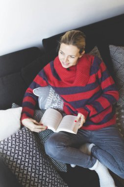 kitap okuma ve evde kanepede otururken gülümseyen mutlu çekici kadın 