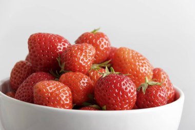 Beyaz arka plan üzerinde izole yıkanmış lezzetli çilek ile beyaz kase yakın çekim