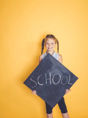 Blackboard kelime okul ile tutarak ve turuncu arka plan önünde poz sarışın kız öğrenci 