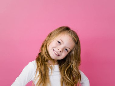 gülümseyen ve kameraya bakarak pembe arka plan beyaz giysili güzel kız portresi 