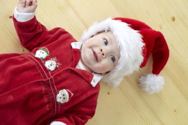 Şirin Bebek gülümseyen ve ahşap yerde yatarken kırmızı Noel Baba kostüm 