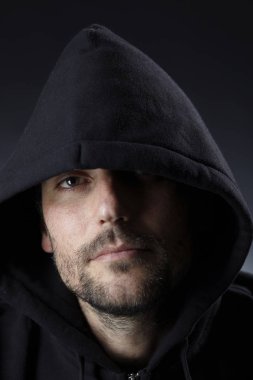 karanlık arka planda kamera bakarak siyah Hood giyen ciddi büyüleyici adam portre 