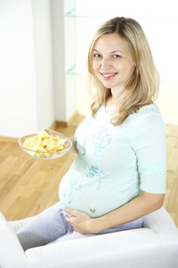 evde mutlu hamile kadın koltukta oturma ve yemek fişleri