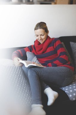 casual kadın dikkatle elbise okuma kitabı evde kanepede otururken 