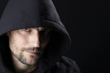 karanlık arka planda kamera bakarak siyah Hood giyen ciddi büyüleyici adam portre 