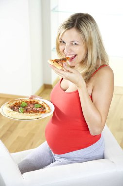 koltukta oturan ve evde pizza yemek mutlu hamile kadın