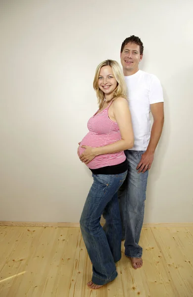 ブロンドの妊娠中の妻と一緒に家の壁の近くでポーズをとって幸せな男 期待コンセプト — ストック写真