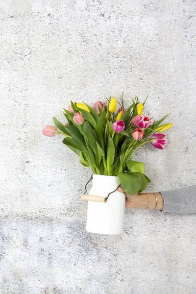 灰色の壁の背景に色とりどりのチューリップと花瓶を持っている女性の手 — ストック写真