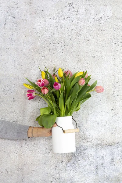 灰色の壁の背景に色とりどりのチューリップと花瓶を持っている女性の手 — ストック写真