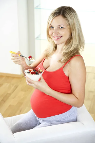 肘掛け椅子に座って 自宅ベリー ヨーグルトで食べて幸せな妊娠中の女性 — ストック写真