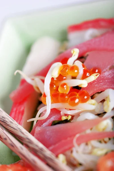 asian fish salad with salmon slices and red caviar with crab sticks and wheat sprouts in plate, close-up