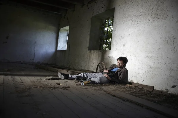 beggar man in dirty clothes lying on floor and sleeping in neglected building