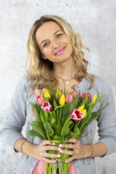 コンクリートの壁の背景 誕生日の概念にポーズのチューリップの花の花束と金髪のスタイリッシュな女性 — ストック写真