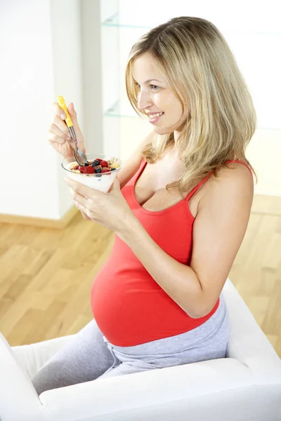 肘掛け椅子に座って 自宅ベリー ヨーグルトで食べて幸せな妊娠中の女性 — ストック写真