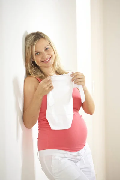 Glad Gravid Kvinna Håller Vita Baby Body Suit Och Lutar — Stockfoto