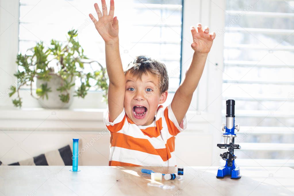 happy boy working with microscope and shouting with raised hands at home