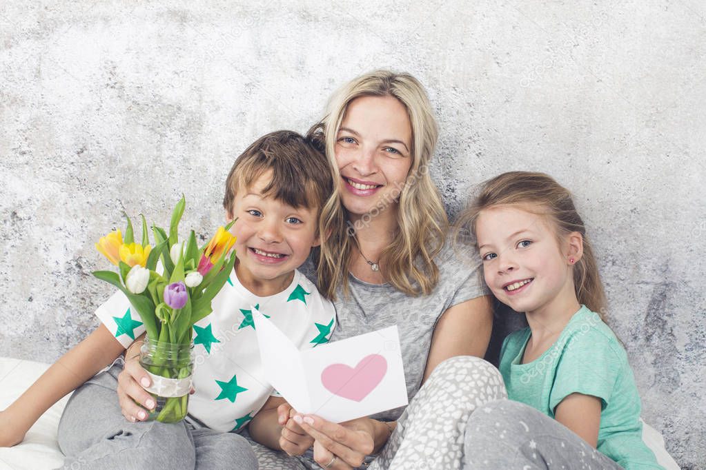Children congratulating young mother with bouquet of tulips and greeting card at Mother Day