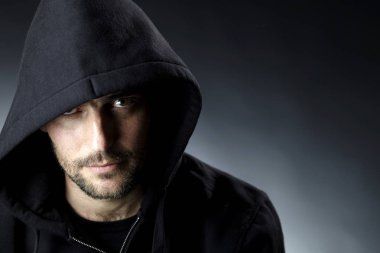 karanlık arka planda kamera bakarak siyah Hood giyen ciddi büyüleyici adam portre 