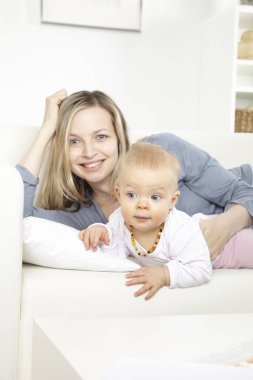 Beyaz koltukta evde bebekle oynarken mutlu genç anne 