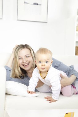 Beyaz koltukta evde bebekle oynarken mutlu genç anne 