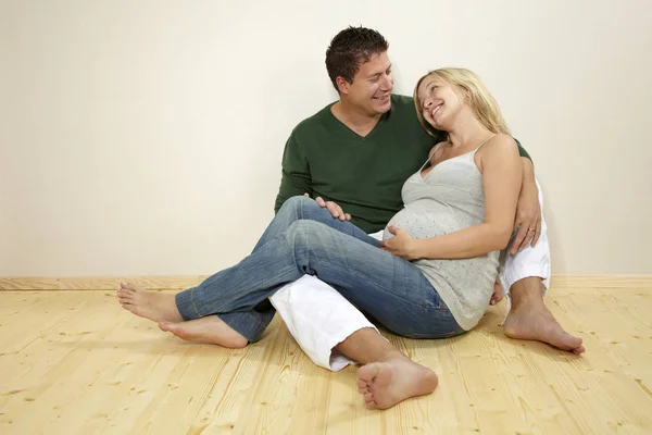 自宅で木製の床の壁の近くに一緒に座って夫と美しい妊娠中の妻 — ストック写真