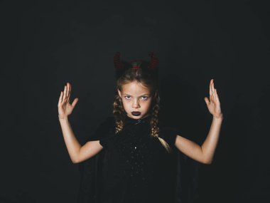 Cadılar Bayramı şeytan küçük kız kostüm kaldırdı elleriyle ayakta ve siyah arka plan üzerine kameraya bakarak kafasına boynuzlarıyla 