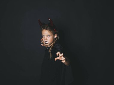 Cadılar Bayramı şeytan küçük kız kostüm kafa ve ağzına kameraya korkutucu hareketi ile seyir siyah arka plan üzerine beyaz yapay sivri boynuzlarıyla 