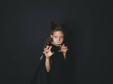 Cadılar Bayramı şeytan küçük kız kostüm kafa ve ağzına kameraya korkutucu hareketi ile seyir siyah arka plan üzerine beyaz yapay sivri boynuzlarıyla 