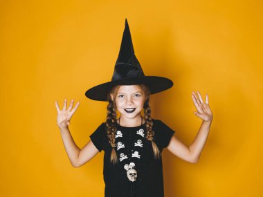 küçük gülümseyen kız halloween cadı kostüm ve siyah şapka ayakta turuncu zemin üzerine kaldırdı kollarını 