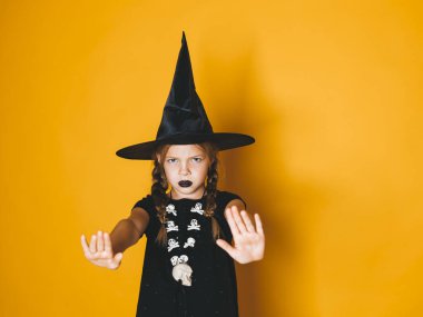 ciddi küçük kız halloween cadı kostüm ve stop jest kamera turuncu arka plan üzerinde gösterilen siyah şapka 