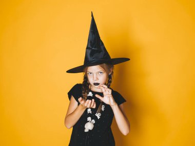 küçük kız halloween cadı kostüm ve siyah şapka kameraya korkutucu hareketi ile turuncu zemin üzerine arıyorum.  