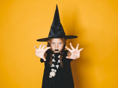 küçük kız halloween cadı kostüm ve siyah şapka kameraya korkutucu hareketi ile turuncu zemin üzerine arıyorum.  