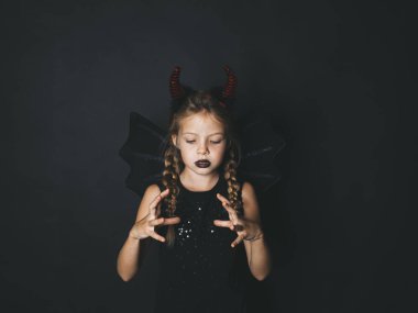 Kız at kuyruklu ve koyu dudaklar ile giyinmiş halloween kılık kırmızı boynuzları ve siyah arka plan üzerine poz kanatlar ile şeytan