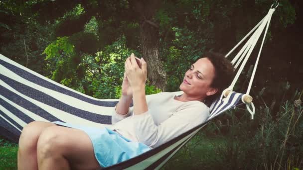 美丽的女人与智能手机放松在方便的吊床上 — 图库视频影像