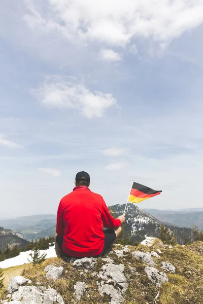 산에서 꼭대기에 앉아있는 국기를 빨간색 스웨터에 등산객 — 스톡 사진