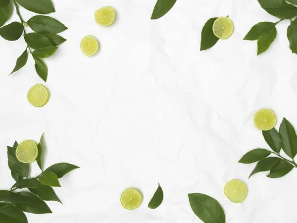 limes and green leaves on white crumpled background