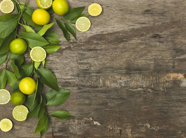 fresh and juicy lemons with limes and green twigs on wooden background