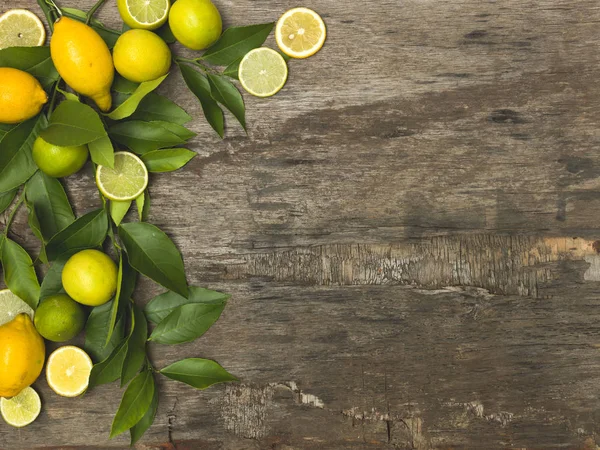 fresh and juicy lemons with limes and green twigs on wooden background