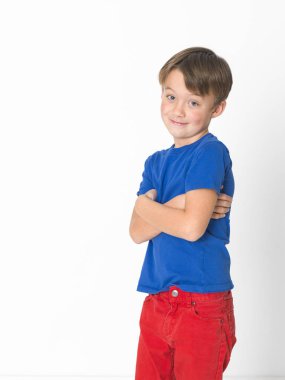 ürkek altı yaşında bir çocuk kırmızı pantolon ve çapraz kolları poz ve kameraya ışık stüdyo özgeçmişlerine bakarak mavi t-shirt 