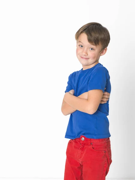 ürkek altı yaşında bir çocuk kırmızı pantolon ve çapraz kolları poz ve kameraya ışık stüdyo özgeçmişlerine bakarak mavi t-shirt 