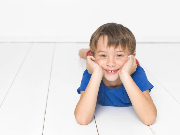 赤いズボンと青 シャツの笑顔と白い木の床に横たわっている間カメラ目線で 歳の少年 — ストック写真