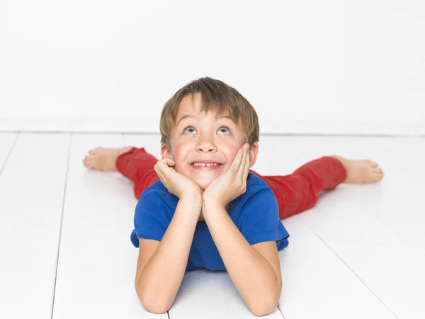 赤いズボンと白い木の床の上に横たわるながら見上げる青い シャツで 歳の少年 — ストック写真