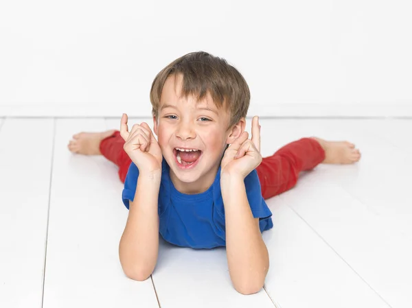 赤いズボンと青 シャツ叫び 白い木の床に横たわっている間指を上向きで 歳の少年 — ストック写真