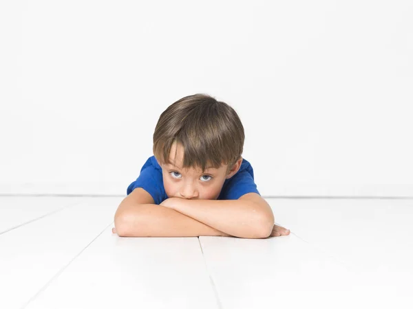 カメラ目線と白い床に組んだ腕を横になっている青い シャツの 歳の男の子 — ストック写真