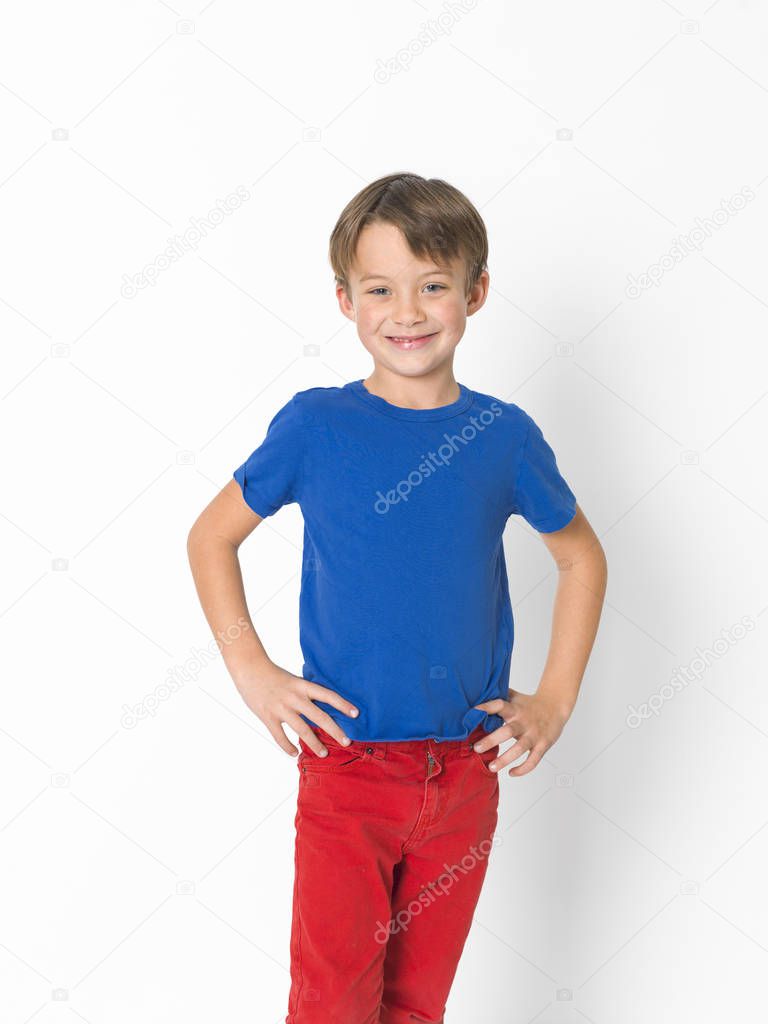 confident six year old boy wearing red trousers and blue t-shirt posing with hands on belt 