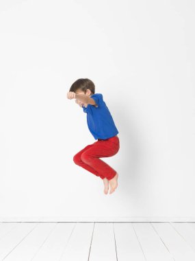 yakışıklı mavi t-shirt ve kırmızı pantolon Studio beyaz duvar önünde ahşap zemin üzerinde yüksek atlama 