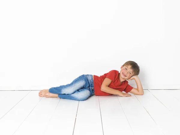 Schattige Blonde Jongen Rood Shirt Blauwe Jeans Liggend Witte Houten — Stockfoto