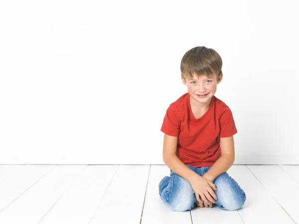 Schattige Blonde Jongen Rood Shirt Blauwe Jeans Zittend Witte Houten — Stockfoto