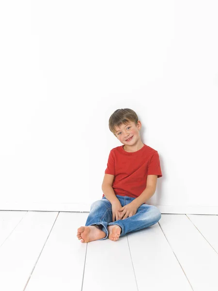 Schattige Blonde Jongen Rood Shirt Blauwe Jeans Zittend Witte Houten — Stockfoto