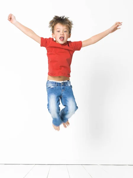Cute Blond Boy Red Shirt Blue Jeans Jumping White Wooden Royalty Free Stock Images